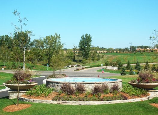 A landscaped area with a circular fountain surrounded by greenery and trees.