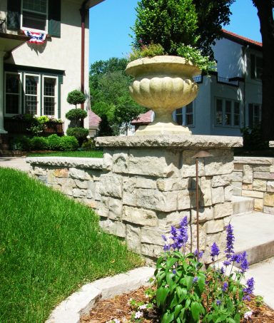 Stone wall with a decorative planter and colorful flowers in a lush garden setting.