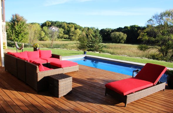 Lounge area with red cushions beside a pool, surrounded by green trees and blue sky.