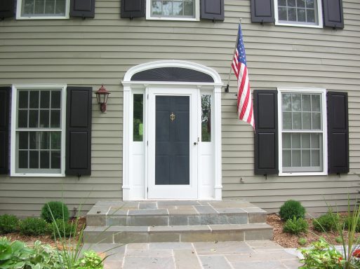 Front entrance of a house with a black door, flanked by windows and an American flag.