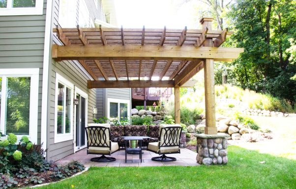 Outdoor patio with a wooden pergola, seating area, and lush greenery in the background.