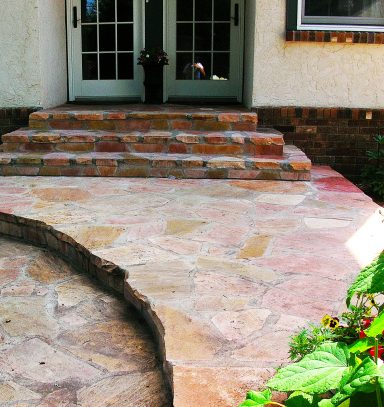Stone pathway leading to double doors with steps and surrounding greenery.