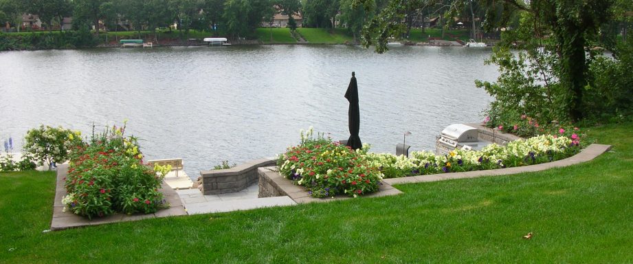Lush garden by a serene lake with flowers and a black umbrella.