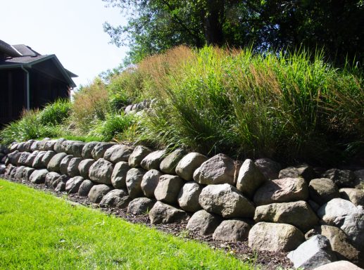 Stone retaining wall with lush green grasses above, set in a grassy area.