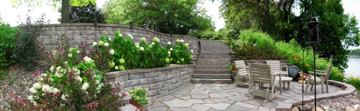 Scenic garden area with stone steps, flowers, and outdoor seating by a water's edge.