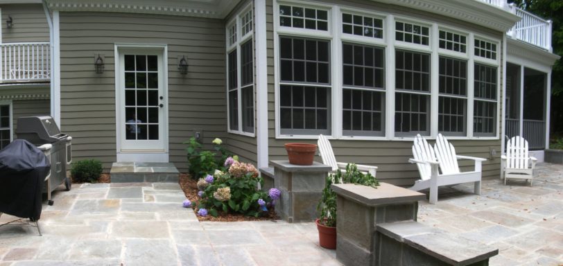 A patio with stone flooring, white chairs, potted plants, and a door leading inside.