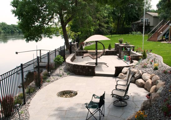 Lakeside patio with seating, curved stone wall, and lush green lawn.