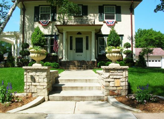 Front steps of a charming house with lush green landscaping and decorative planters.