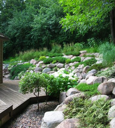 Lush garden slope with greenery, rocks, and wooden pathway.